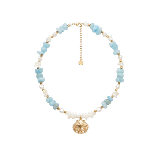 A delicate beaded necklace featuring light blue and white beads with gold spacer beads, a gold chain extender, and a gold seashell charm, displayed on a clean white background.